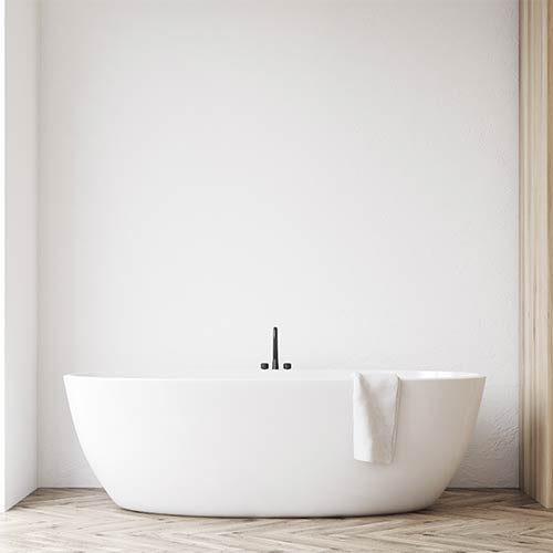 White freestanding bathtub with a white towel draped over the edge in a minimalist bathroom.