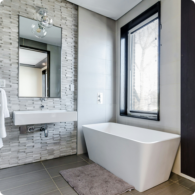 Modern bathroom with a white freestanding bathtub, rectangular sink, gray tile floor, textured gray wall, and a window with blinds.