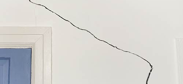 White wall with a long diagonal crack running from top left to bottom right near a partially visible blue door frame.