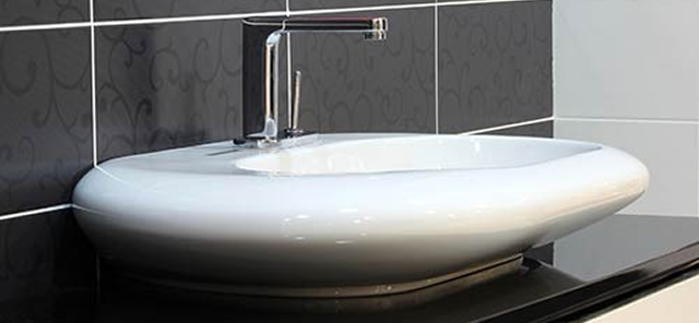 Modern white oval bathroom sink with a chrome faucet mounted on a black countertop against a black and white tiled wall.