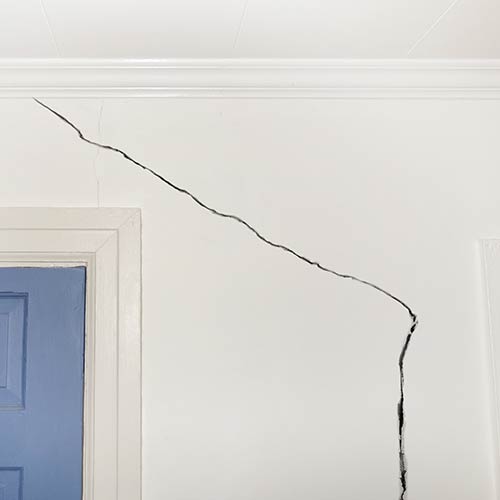 Large diagonal crack running across a white interior wall near a blue door frame.