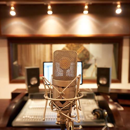 Close-up of a professional studio microphone with a sound mixing console and speakers in the background.