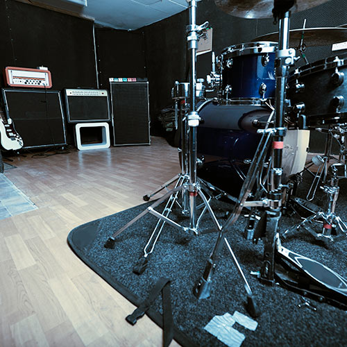 Music rehearsal room with a drum set on a rug and amplifiers with an electric guitar against the wall.