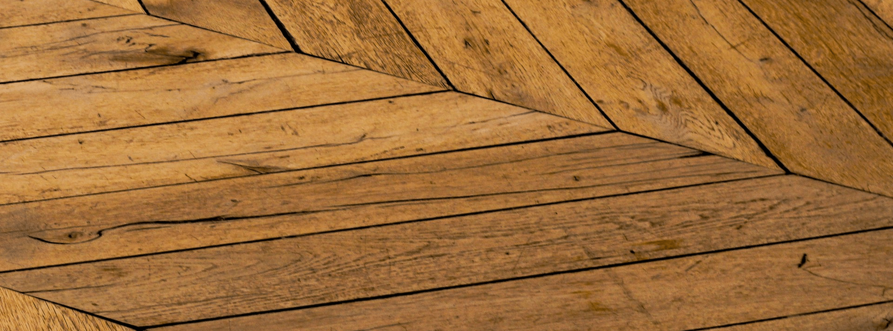 Close-up of wooden floor panels arranged in a herringbone pattern with visible grain and texture.