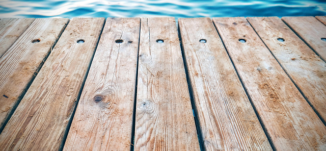 Close-up of weathered wooden dock planks with blue water in the background.