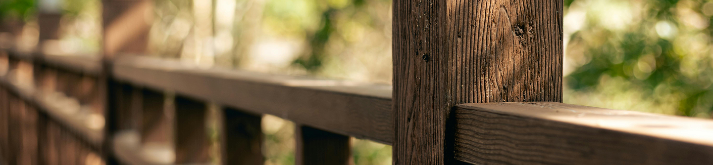 Close-up of a wooden fence railing with blurred trees in the background.