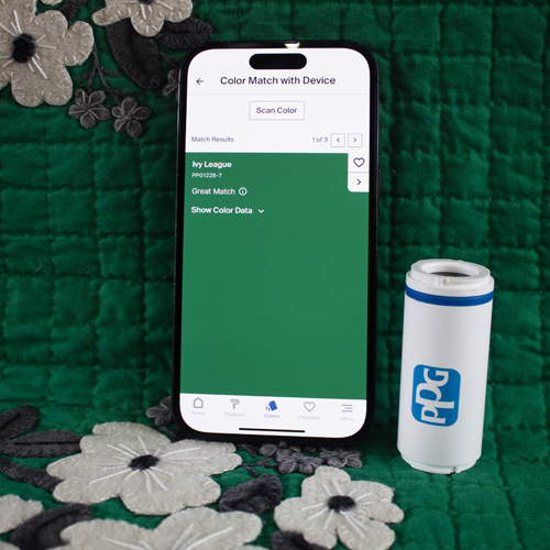 Smartphone displaying a color matching app with 'Ivy League' green color selected, next to a white cylindrical PPG device on a green quilted floral fabric background.
