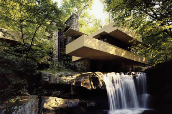 Modern house built over a waterfall surrounded by dense green trees in a forest.