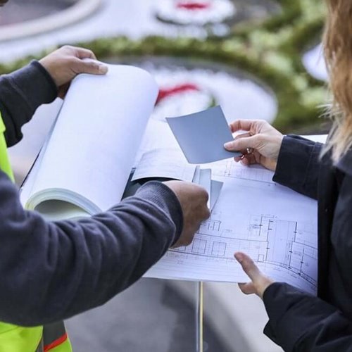 Two people reviewing architectural blueprints outdoors, one holding a color sample card.