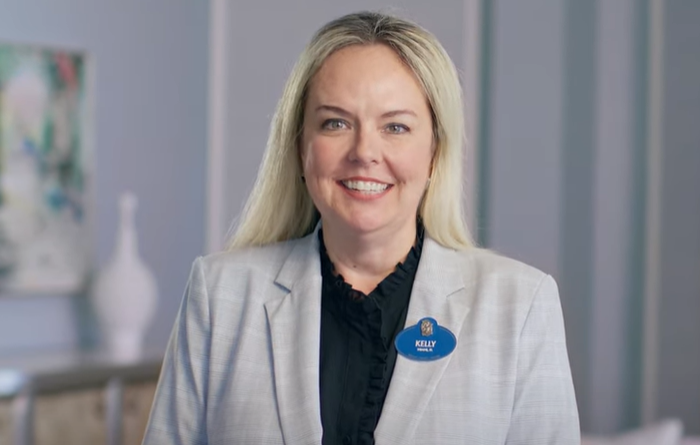 Smiling woman with long blonde hair wearing a light gray blazer and a name badge that reads 'Kelly'.