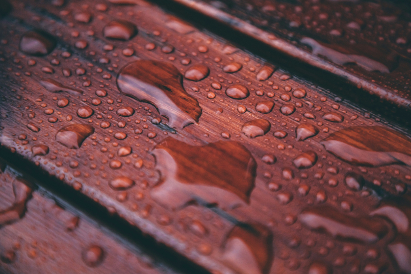 Close-up of water droplets on a polished wooden surface with visible wood grain.