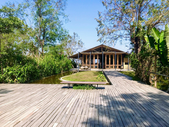 Modern wooden house surrounded by trees with a large wooden deck and narrow water features.