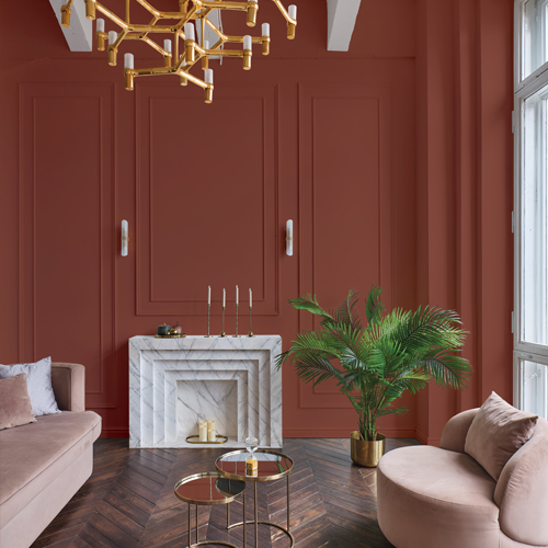 Elegant living room with a round velvet sofa, beige couch, marble fireplace, green potted plant, and gold accents under a modern chandelier.