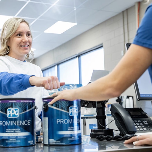 A customer smiling while purchasing PPG Prominence interior paint at a counter with a sales associate.