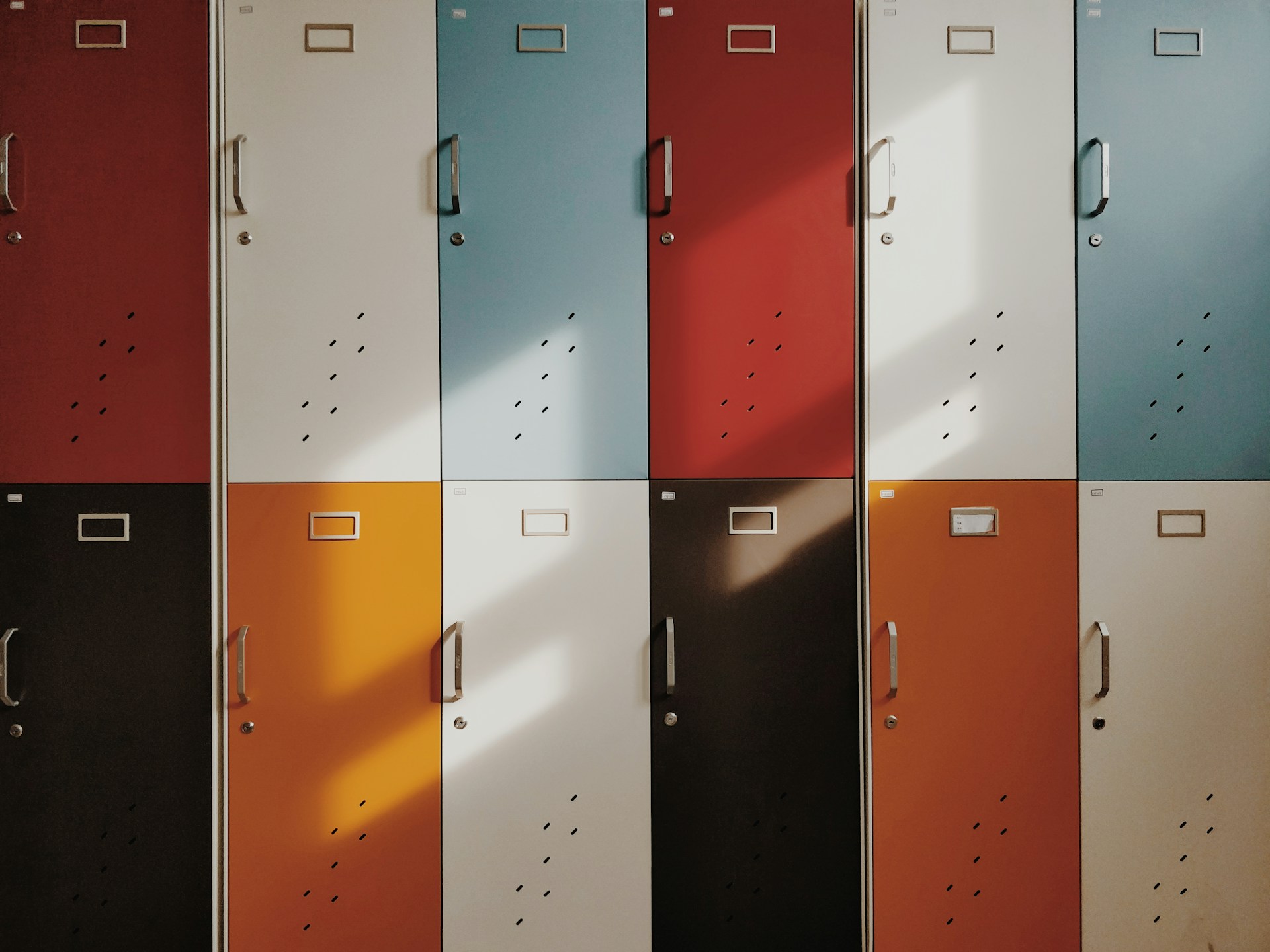 Rows of colorful metal lockers in shades of red, white, blue, black, and orange with sunlight casting shadows.