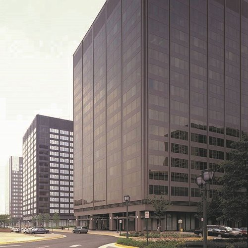 Modern glass and concrete office buildings along a curved street with parked cars and street lamps.