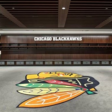 Empty Chicago Blackhawks hockey locker room with team logo on the floor and 'CHICAGO BLACKHAWKS' sign on the wall.
