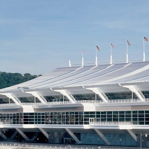 Modern stadium with a white curved roof and American flags on top against a clear blue sky.