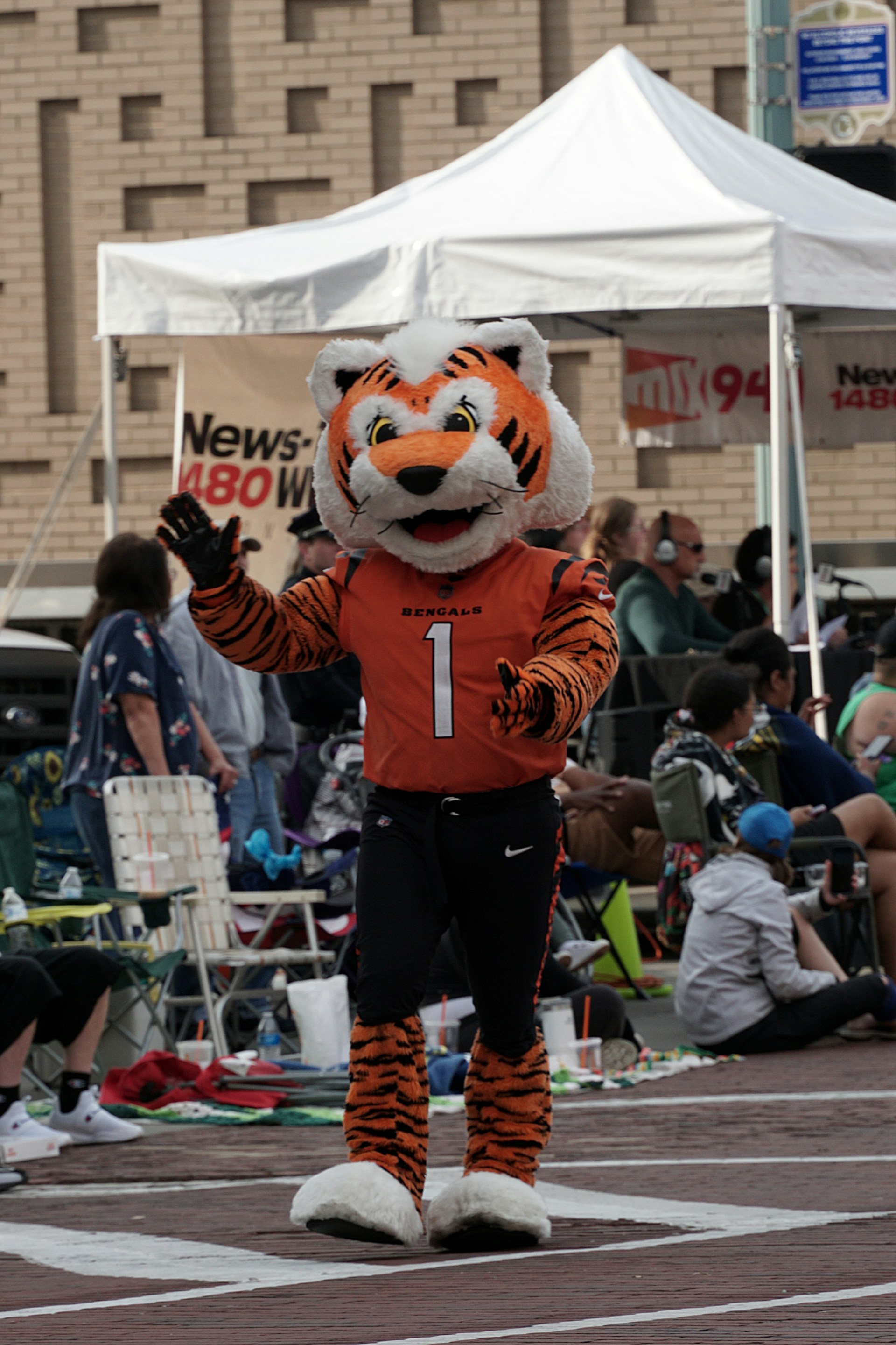 Cincinnati Bengals mascot in orange and black costume waving during an outdoor event with spectators in the background.