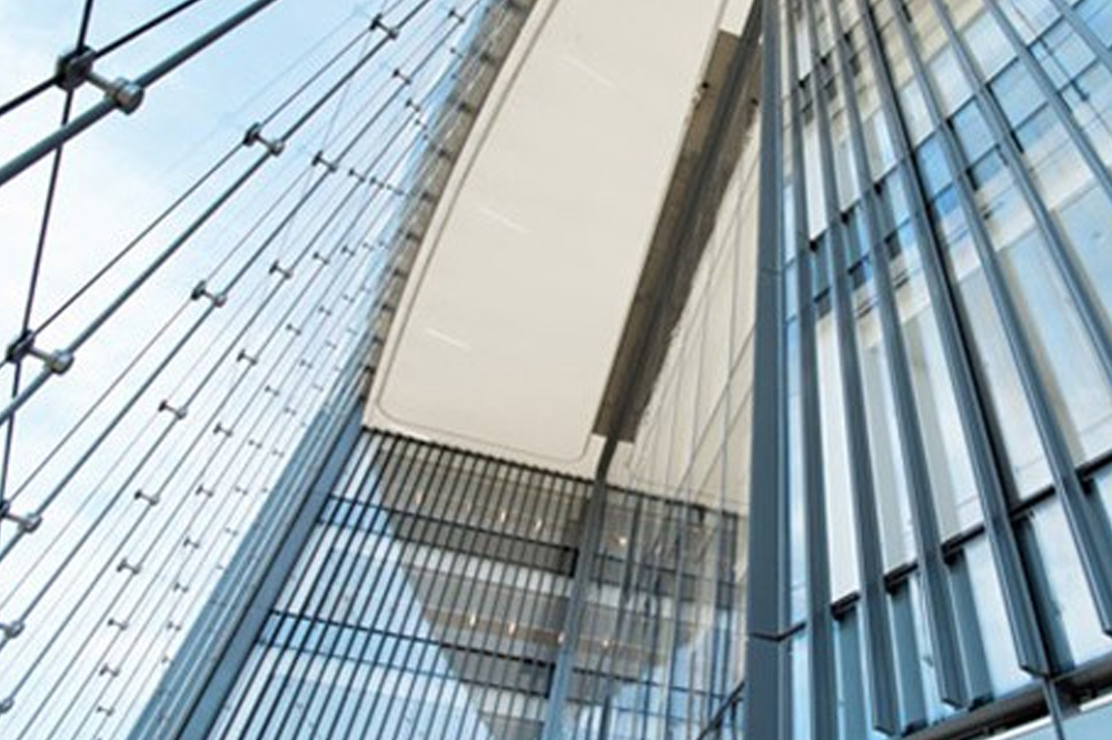Close-up view looking up at a modern glass building facade with metal framework and cables.