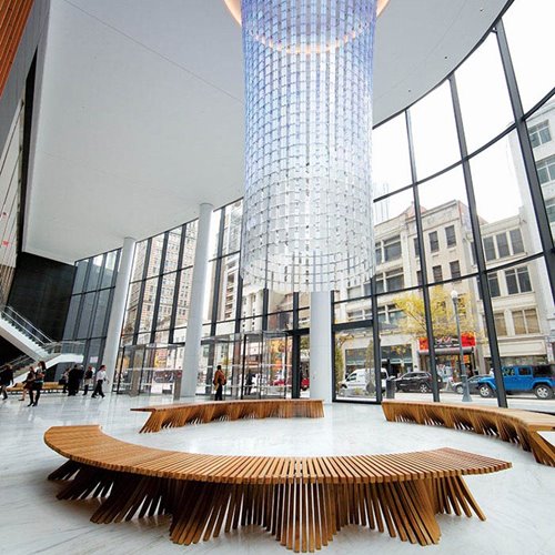 Modern spacious lobby with floor-to-ceiling windows, curved wooden benches, and a large cylindrical chandelier.