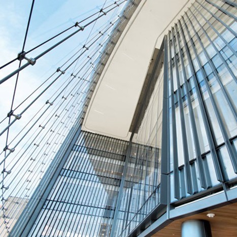 Upward view of a modern building facade with large glass panels and vertical metal slats under a blue sky.