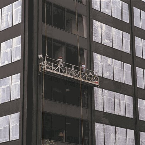 Two workers on a suspended scaffold cleaning or maintaining windows of a tall dark building.