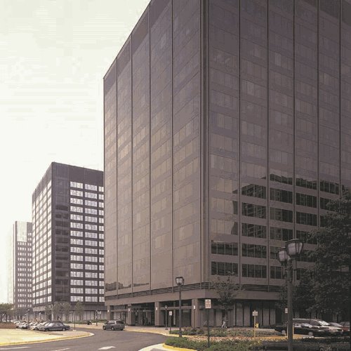 Wide street view of modern glass office buildings under overcast sky with cars parked along the curb.