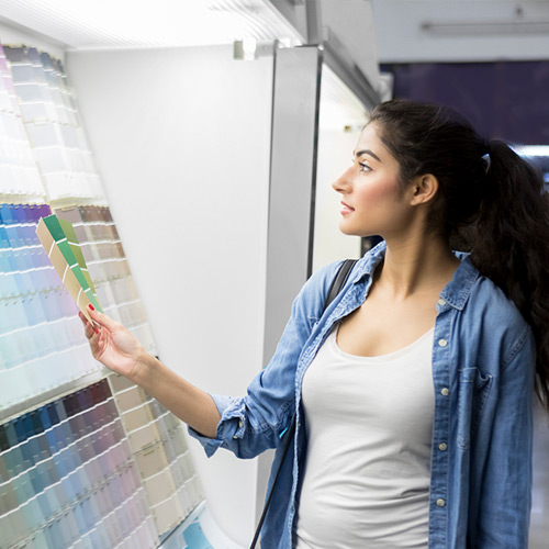 Woman in casual clothes holding paint color swatches and looking at a wall of paint samples.