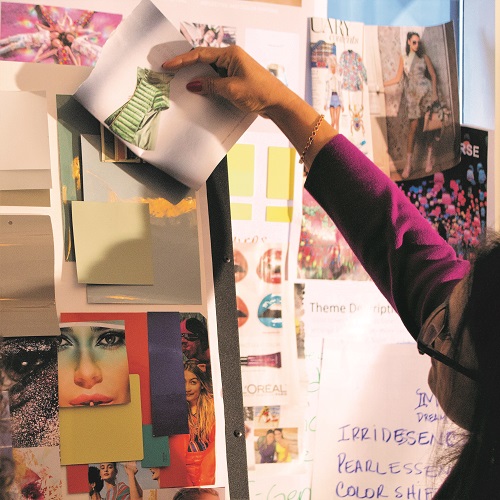 Person wearing a purple sleeve pointing to a green and white striped dress photo on a collage board filled with fashion images and color swatches.