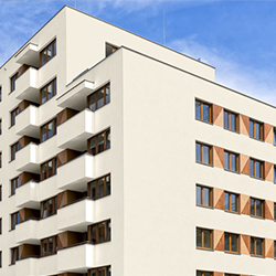 Modern white apartment building with balconies and wooden window shutters against blue sky.