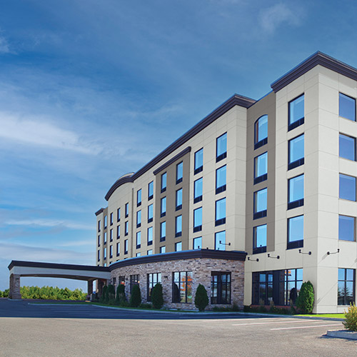 Modern four-story hotel building with large windows and stone accents under a blue sky.