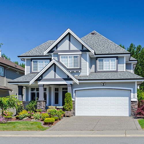 Modern two-story house with gray siding, white garage door, and a landscaped front yard under a clear blue sky.