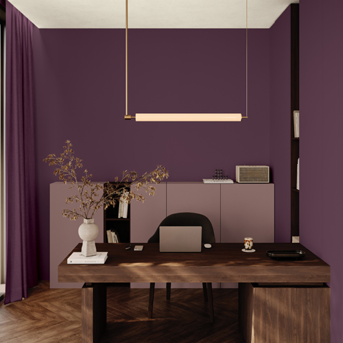 Modern home office with purple walls, a wooden desk with laptop, chair, decorative vase, and a hanging light fixture.