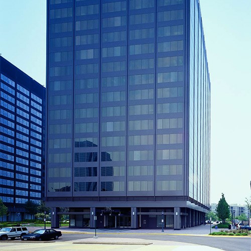 Modern office building with reflective glass windows and a columned base on a city street corner.