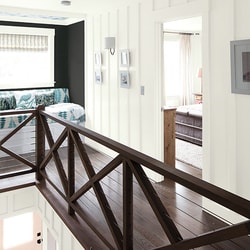 Interior view of a modern home hallway with dark wooden railing and white walls, leading to a bedroom and living area.