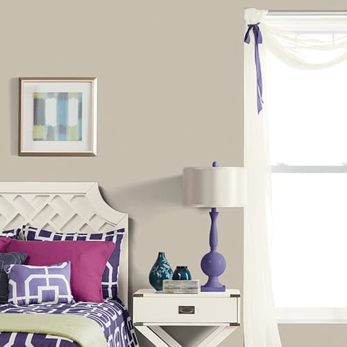Modern bedroom corner with a white lattice headboard bed featuring purple and pink pillows, a white nightstand with blue vases, a purple lamp, and sheer white curtains tied with a purple ribbon.