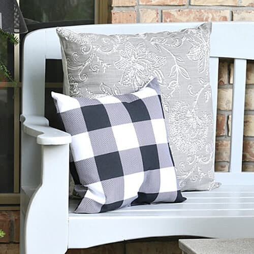 White wooden bench with a large gray floral cushion and a smaller black and white checkered cushion.