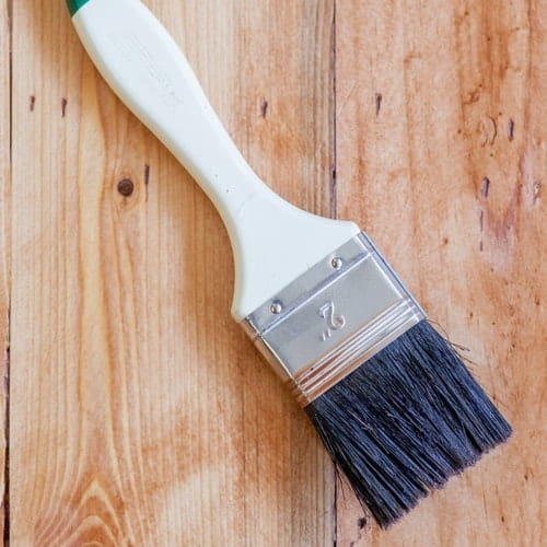 Paintbrush with white handle and black bristles resting on a wooden surface.
