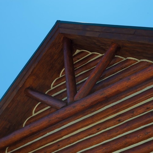 Close-up of a wooden log cabin roof with diagonal logs and clear blue sky background.