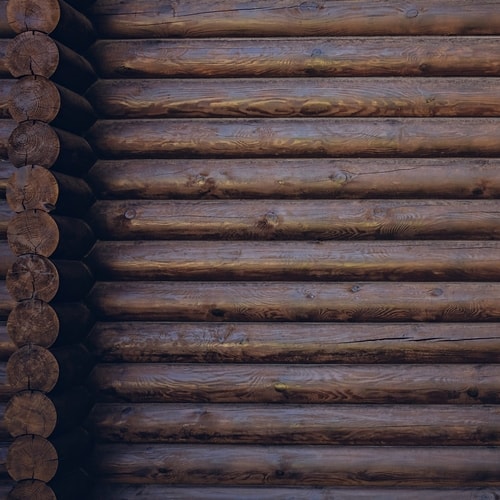Close-up view of dark brown horizontal wooden logs stacked with rounded ends visible on the left side.