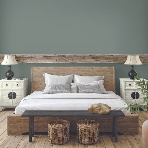 Rustic bedroom with a wooden bed frame, white bedding, two nightstands with lamps, a bench with woven baskets underneath, and light green walls.