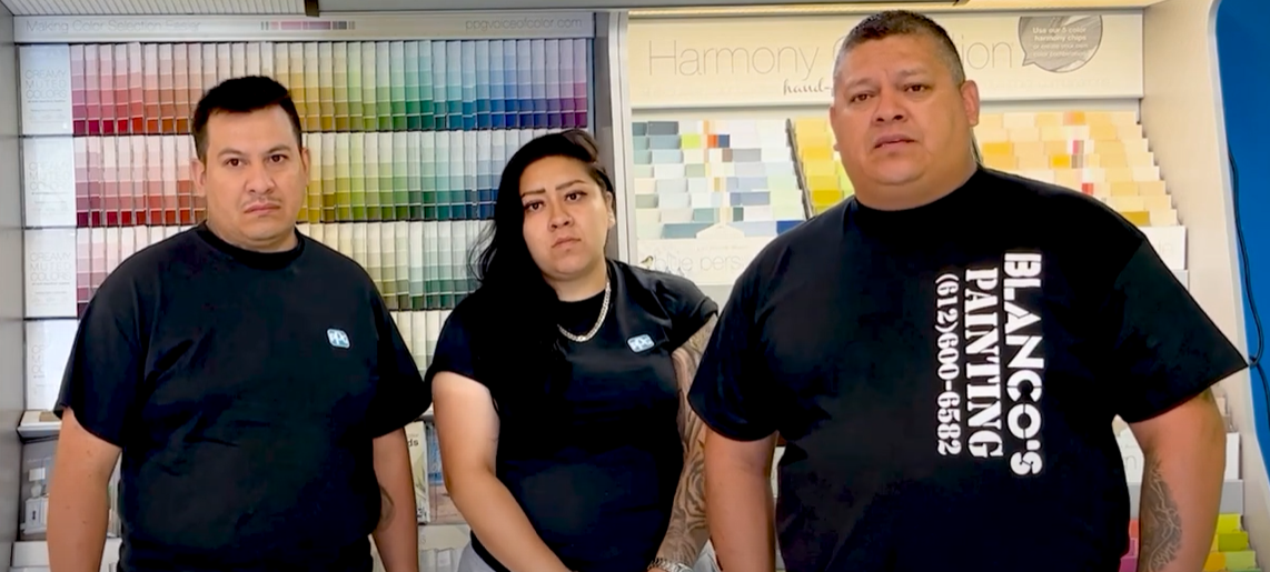 Three people wearing black shirts standing in front of a wall with various paint color samples, one shirt displays Blanco's Painting logo and phone number.