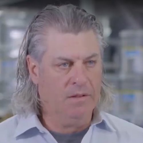 Middle-aged man with slicked-back gray hair and blue eyes wearing a light blue collared shirt.
