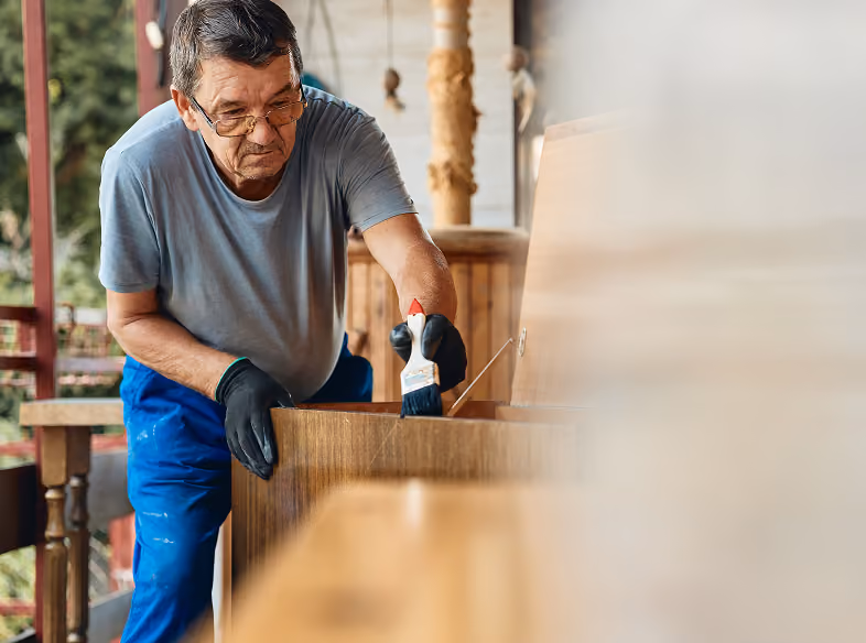A wood craftsman applying coating to a wooden chest with a brush