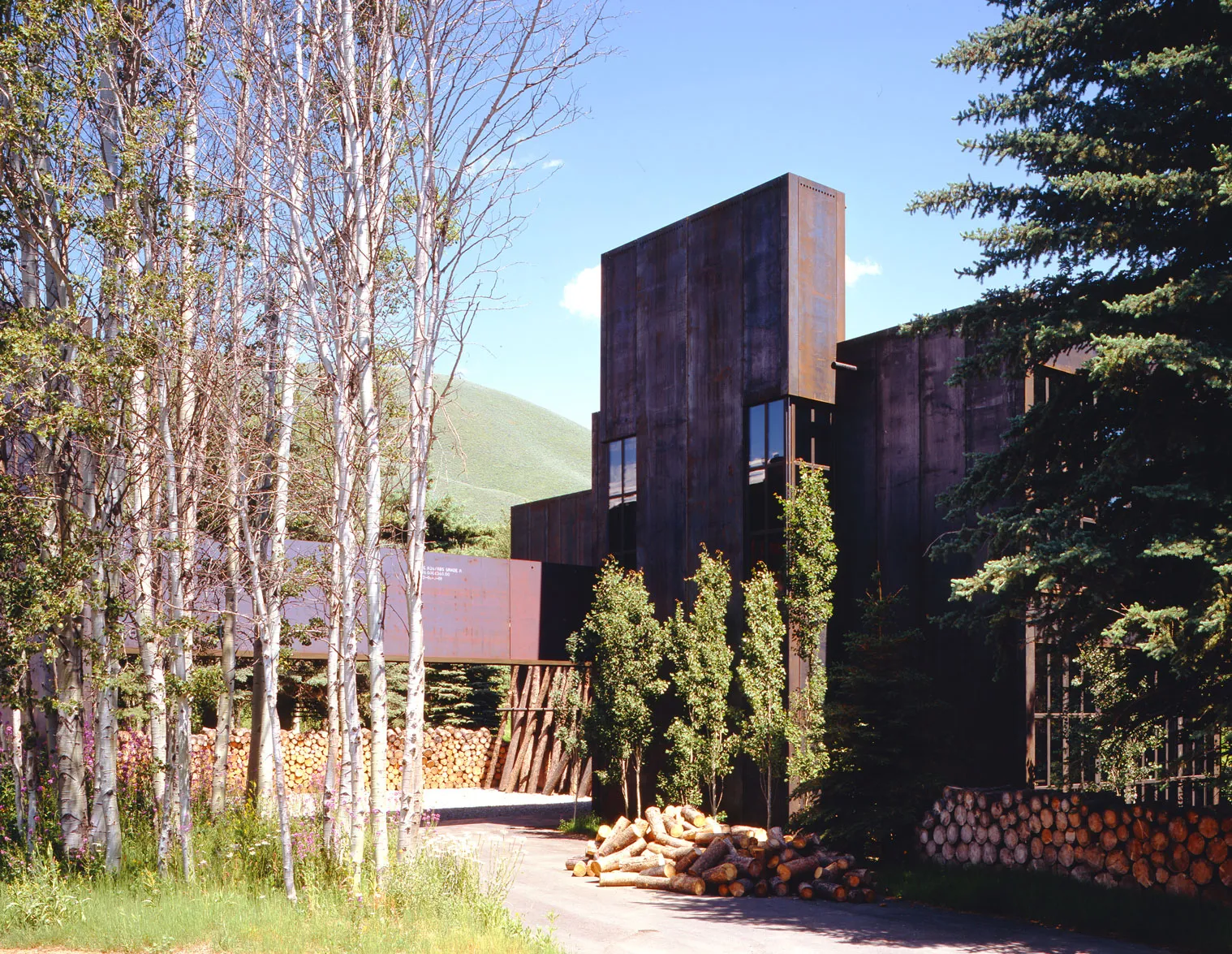 Exterior of the Steel House in Sun Valley, Idaho, featuring tall weathered steel walls, vertical windows, and surrounding aspen trees, designed by Susan Desko.