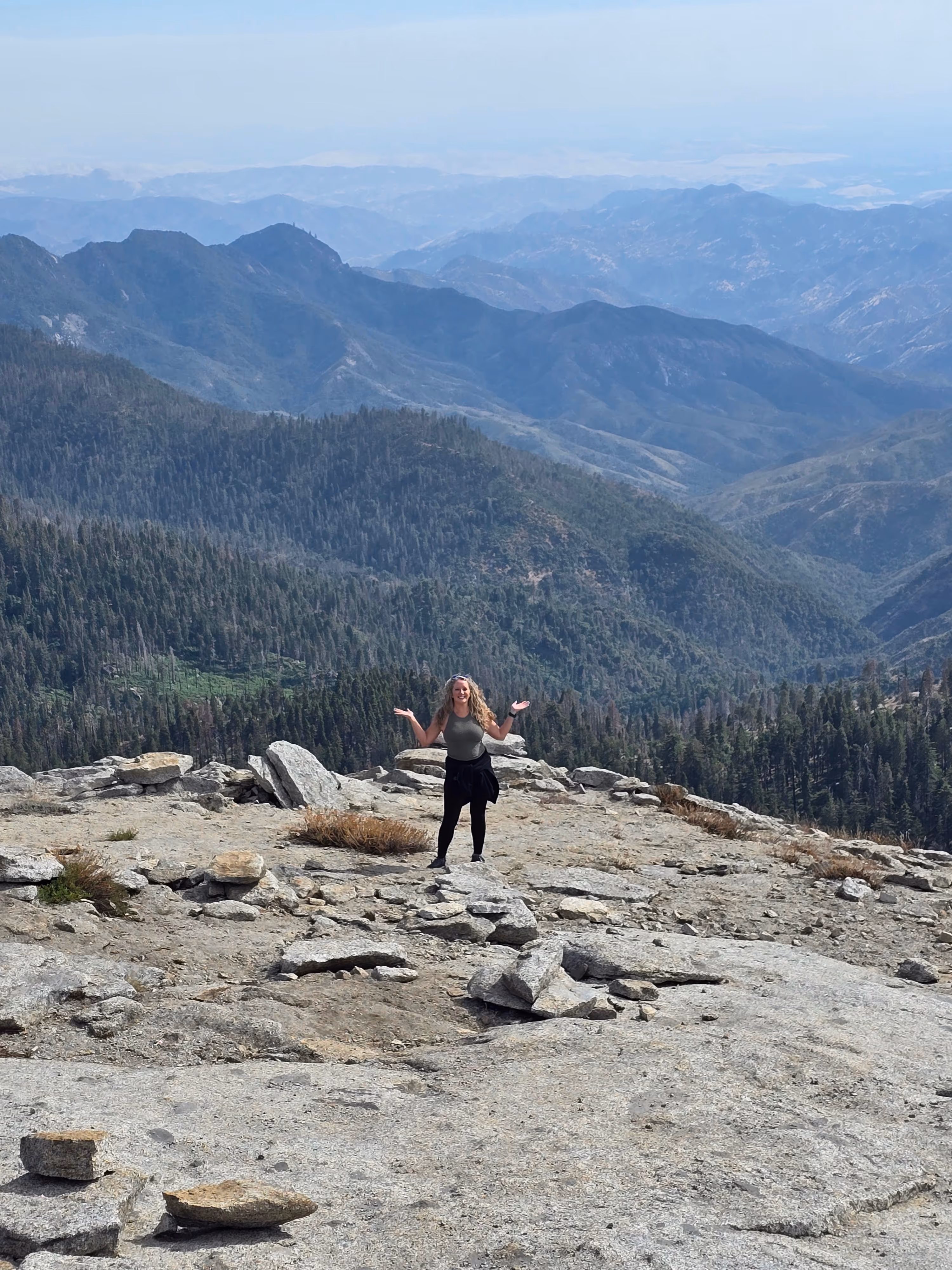 Marcia Foster standing on mountain peak overlooking layered mountain ranges in the distance