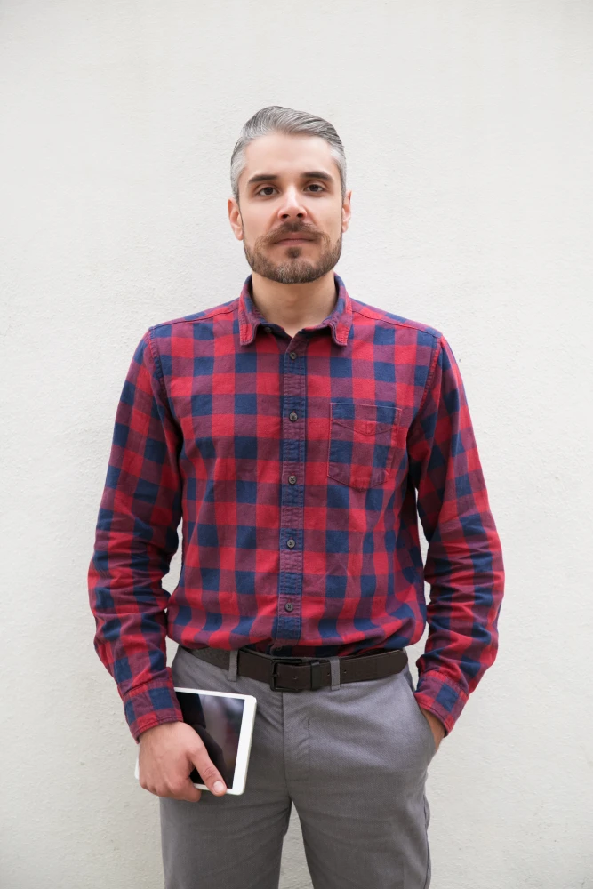 Portrait of man in red plaid shirt standing with arms crossed.