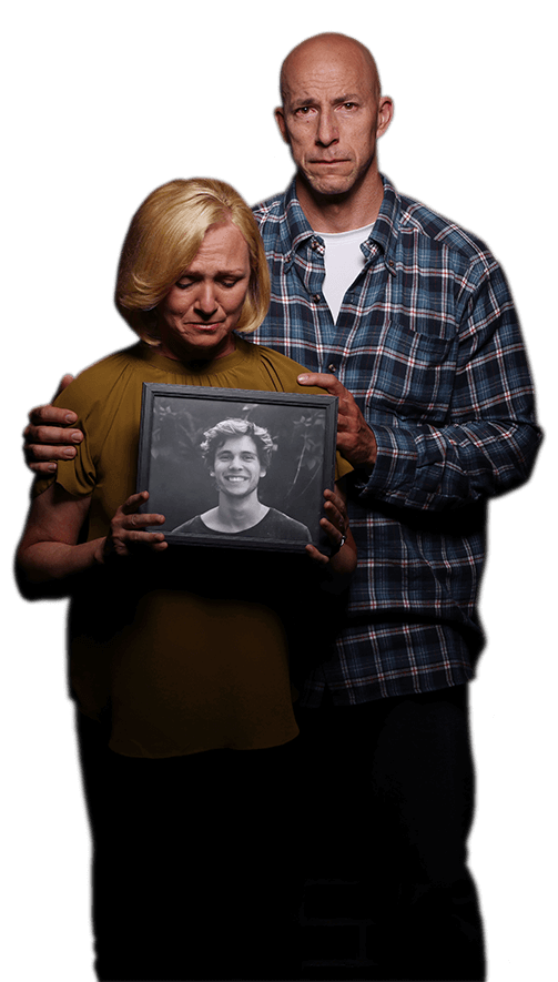 A mother and a father holding a photograph of their son, looking sad