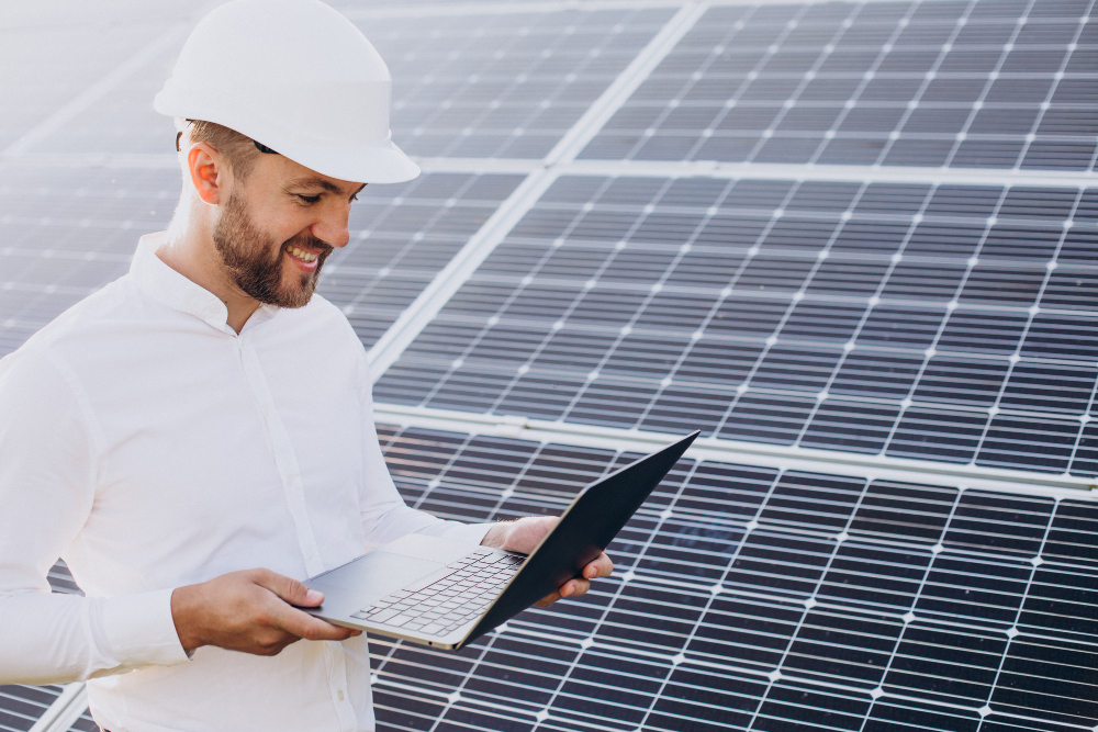 Techniker mit Schutzhelm und Laptop vor Solarmodulen